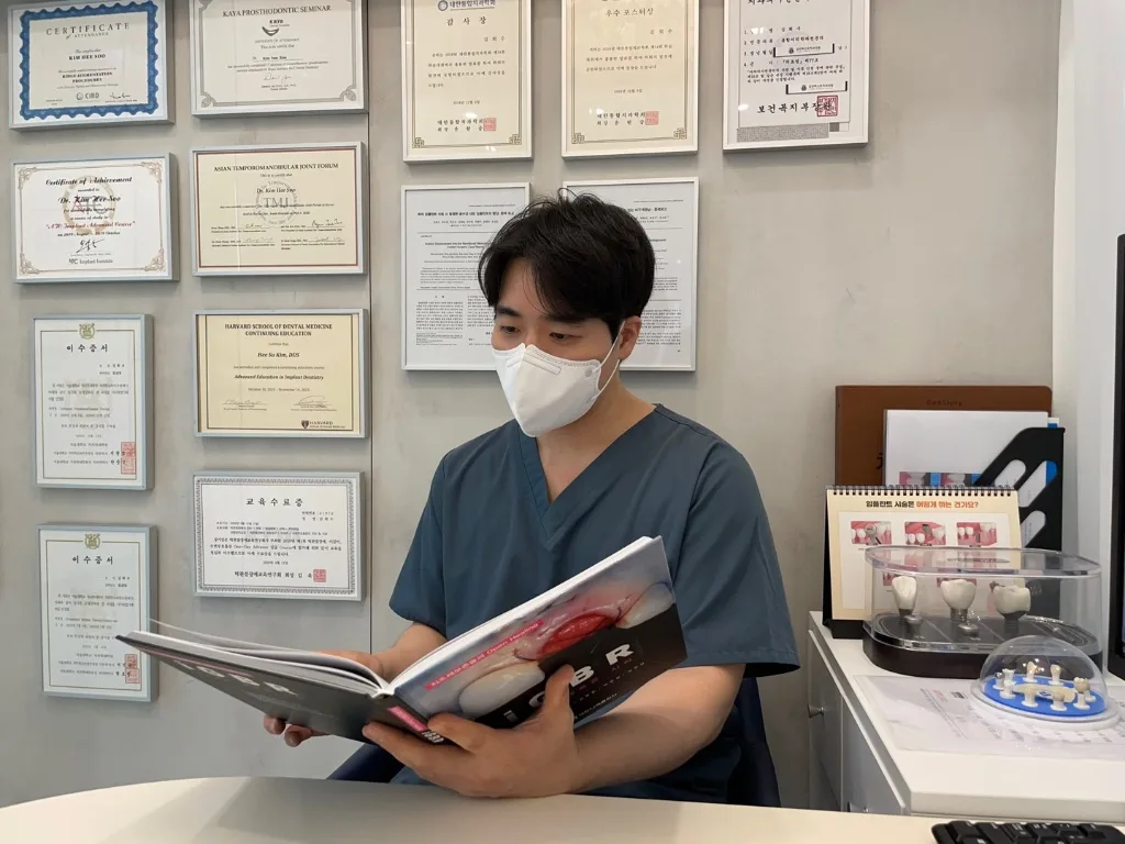 수료증과 인증서 앞에서 임상 서적을 연구하는 김희수 원장